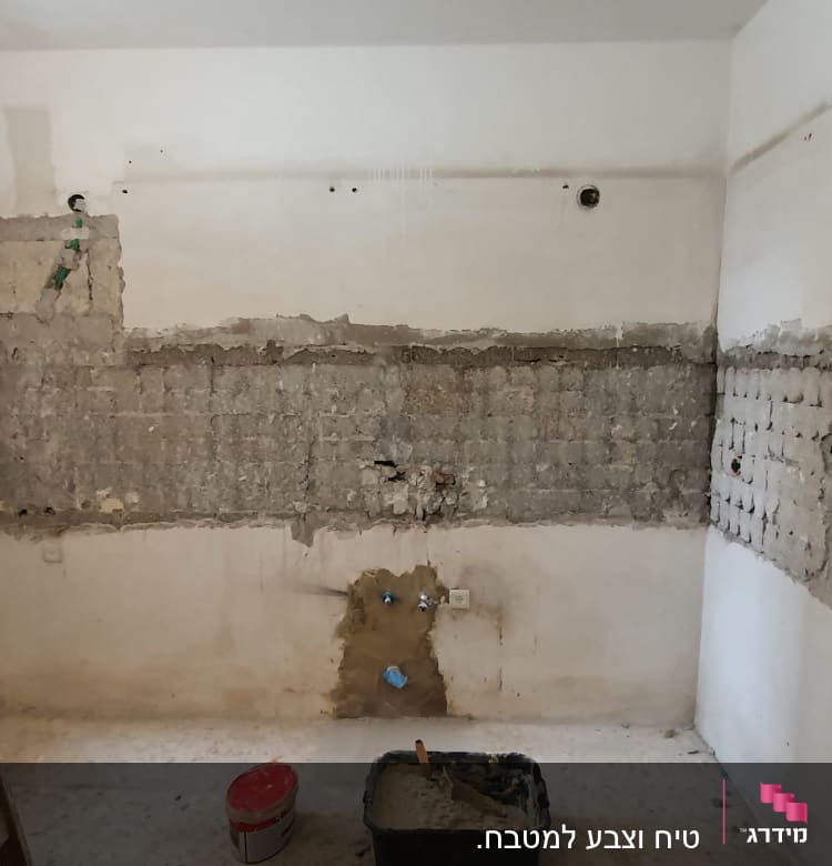 קיר עם טיח מתקלף ודלי צבע על הרצפה